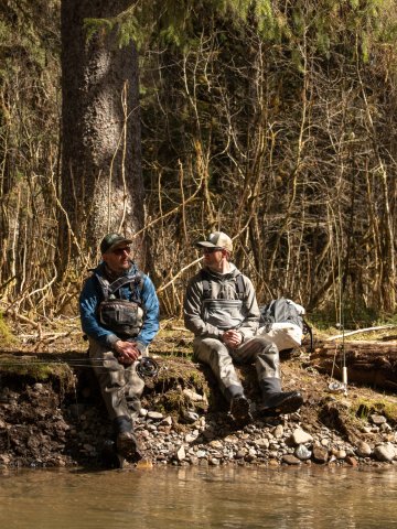 Two anglers resting on a forested riverbank