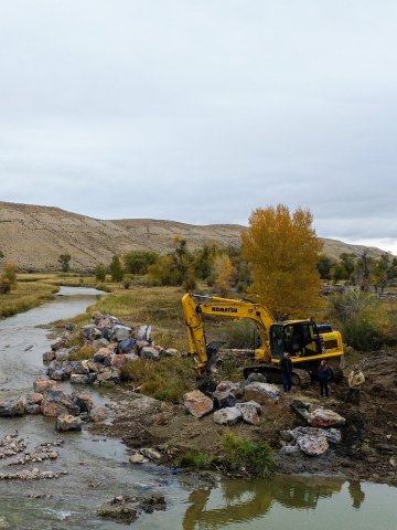 Excavator placing boulders in a river restoration site