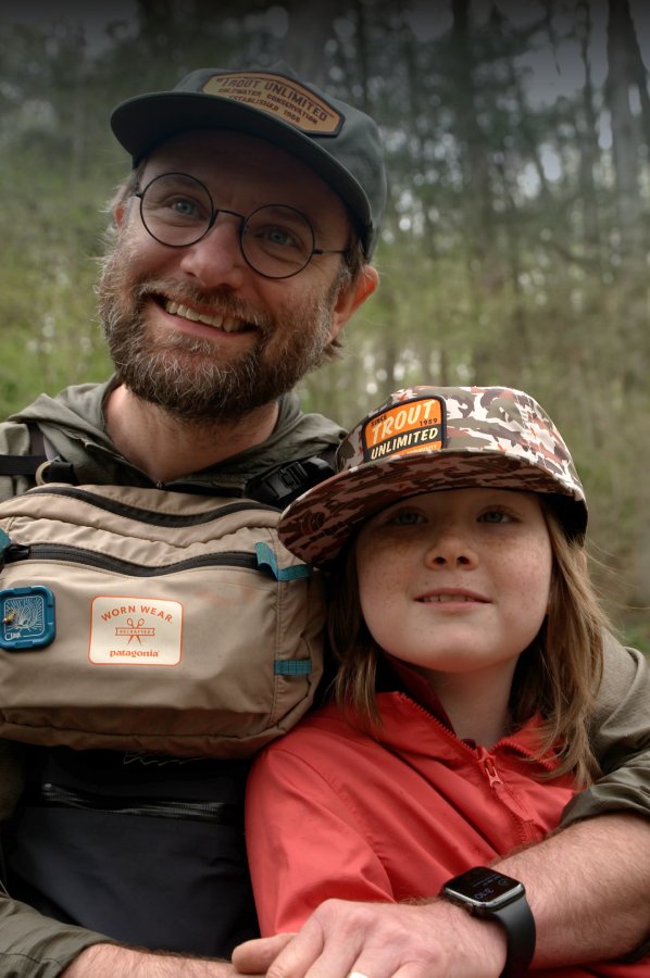 A father and daughter in Trout Unlimited caps, smiling at the camera