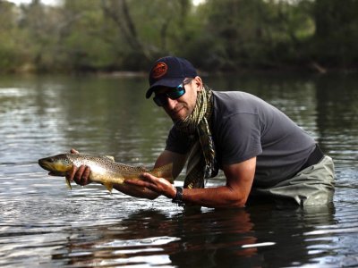 Angler kneeling in a river holding a brown trout